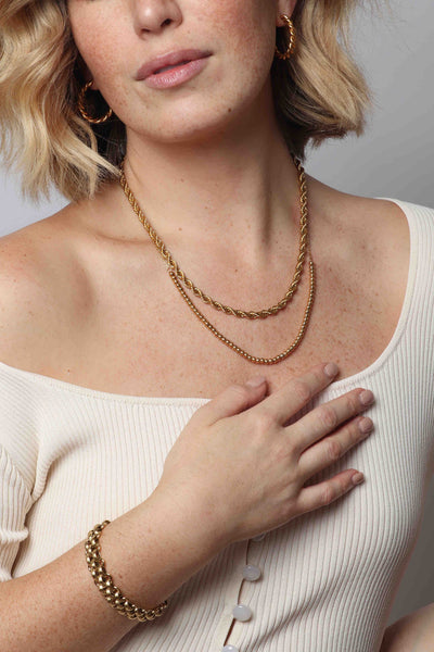 Layered 14k gold stainless steel hypoallergenic water resistant waterproof jewelry by Marrin Costello that will not turn your skin green including our twisted Rita Hoops, twisted rope Helix Chain in 5mm width, 4mm beaded chain adjustable Crown Chain necklace, thick textured Lattice XL Bracelet, paired with a ribbed button down ivory top from Canvas Fashion Gallery.